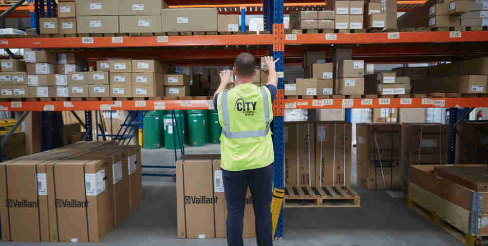 A man in a City Plumbing hi vis vest inspects boxes in a warehouse